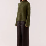 Woman wearing a green sweater and black pants on a white background