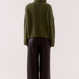 Person wearing a green sweater and dark pants on a white background