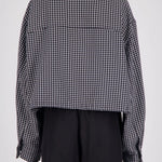 Back view of a person wearing a cropped black and white gingham long-sleeve shirt with black trousers, shown against a plain light gray studio background.