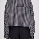 Back view of a person wearing a cropped black and white gingham long-sleeve shirt with black trousers, shown against a plain light gray studio background.