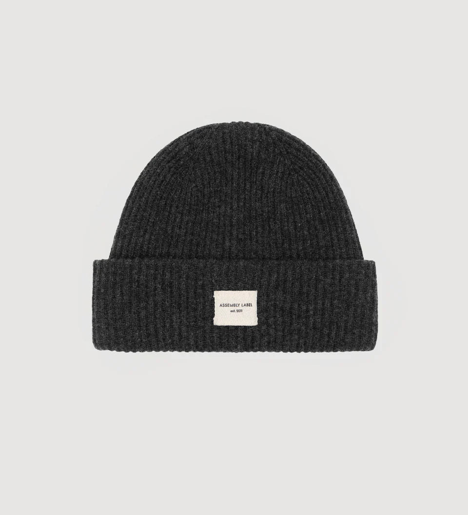 Black knit beanie with a small white label on a light gray background