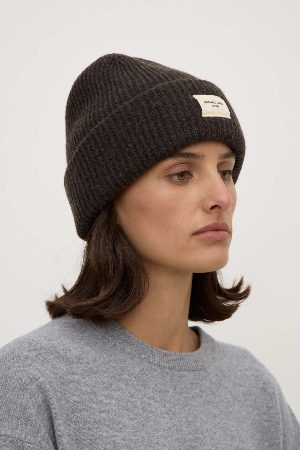 Woman wearing a dark knit beanie with a logo on a white background