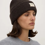 Woman wearing a dark knit beanie with a logo on a white background