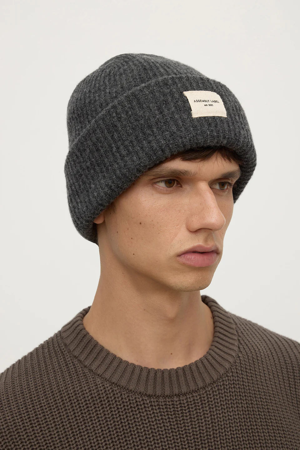 Man wearing a gray knit beanie with a brand logo on a plain background
