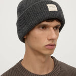 Man wearing a gray knit beanie with a brand logo on a plain background