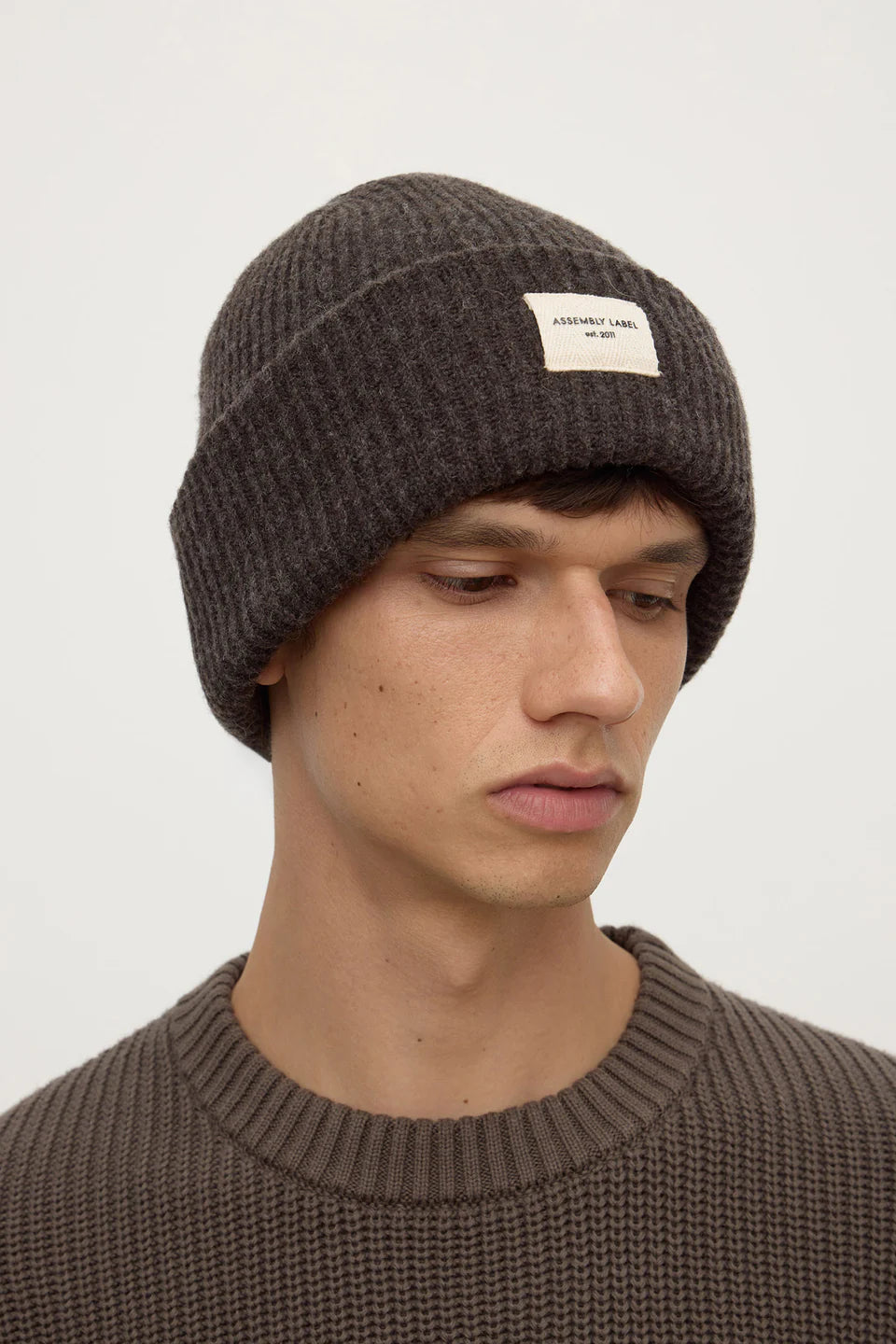 Man wearing a brown knit beanie with a small logo on a white background