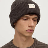 Man wearing a brown knit beanie with a small logo on a white background