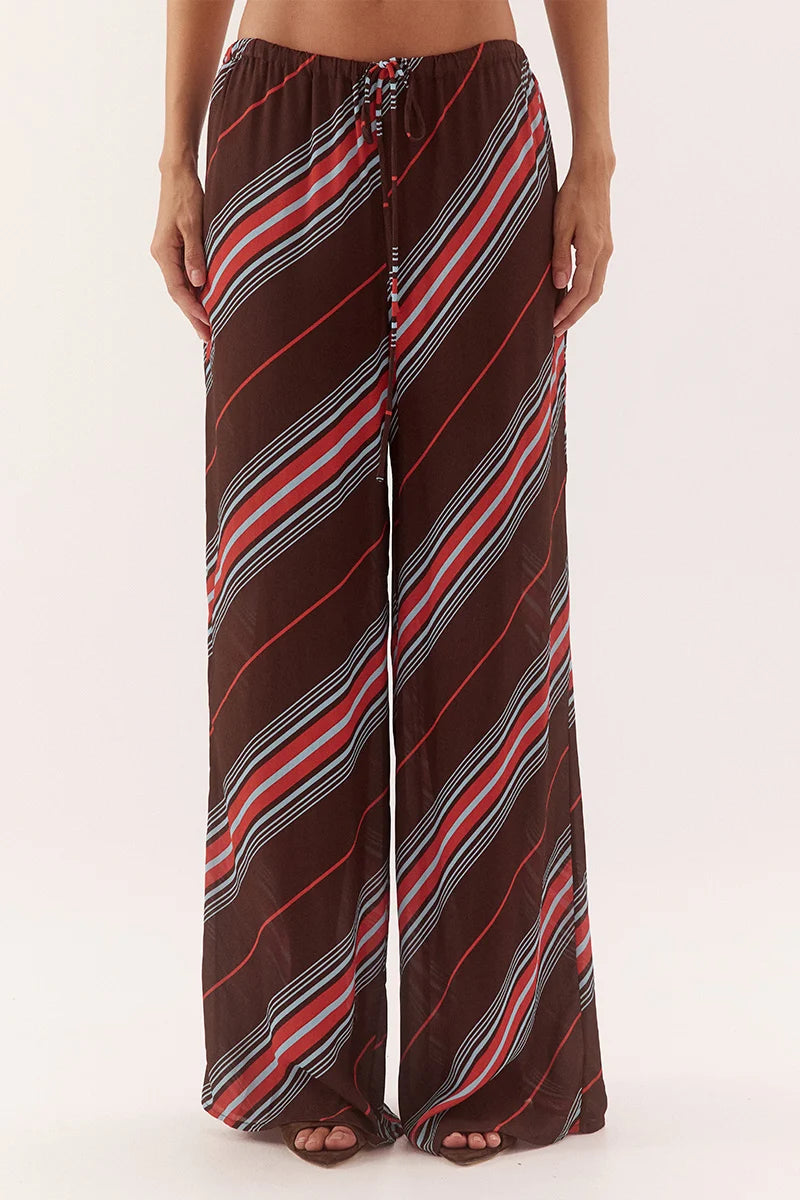 A person wearing loose, wide-leg drawstring pants with diagonal stripes in brown, red, white, and gray, shown from the waist down against a plain light background.