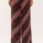 A person wearing loose, wide-leg drawstring pants with diagonal stripes in brown, red, white, and gray, shown from the waist down against a plain light background.