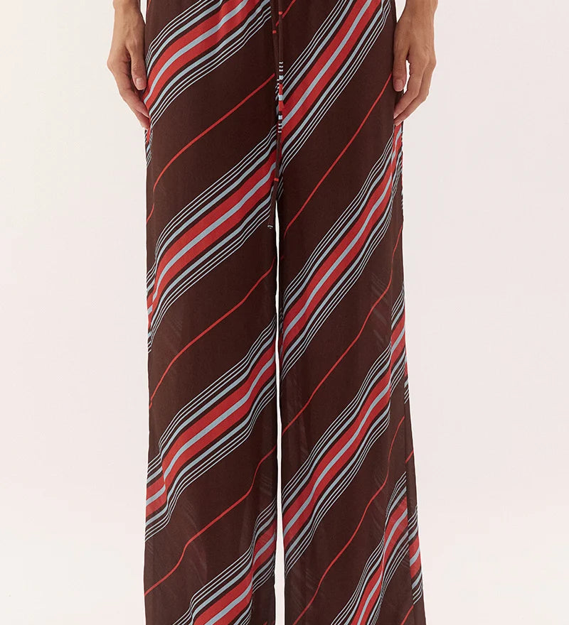A person wearing loose, wide-leg drawstring pants with diagonal stripes in brown, red, white, and gray, shown from the waist down against a plain light background.