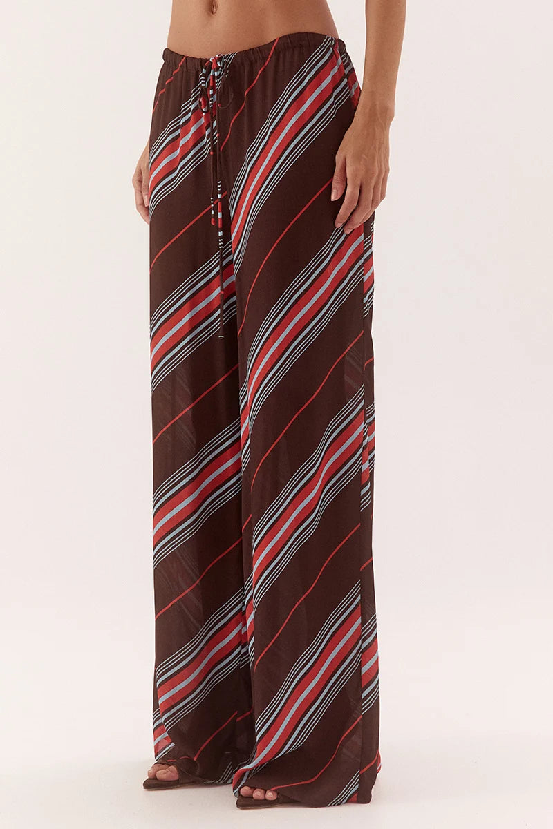 A person wearing loose, wide-leg pants with diagonal stripes in dark brown, red, white, and black, shown from the waist down against a plain light background.
