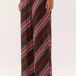 A person wearing loose, wide-leg pants with diagonal stripes in dark brown, red, white, and black, shown from the waist down against a plain light background.