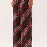 A person wearing loose, wide-leg pants with diagonal stripes in dark brown, red, white, and black, shown from the waist down against a plain light background.
