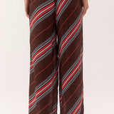 A person wearing loose, wide-leg pants with a diagonal striped pattern in dark brown, red, white, and gray, shown from the waist down against a plain light background.