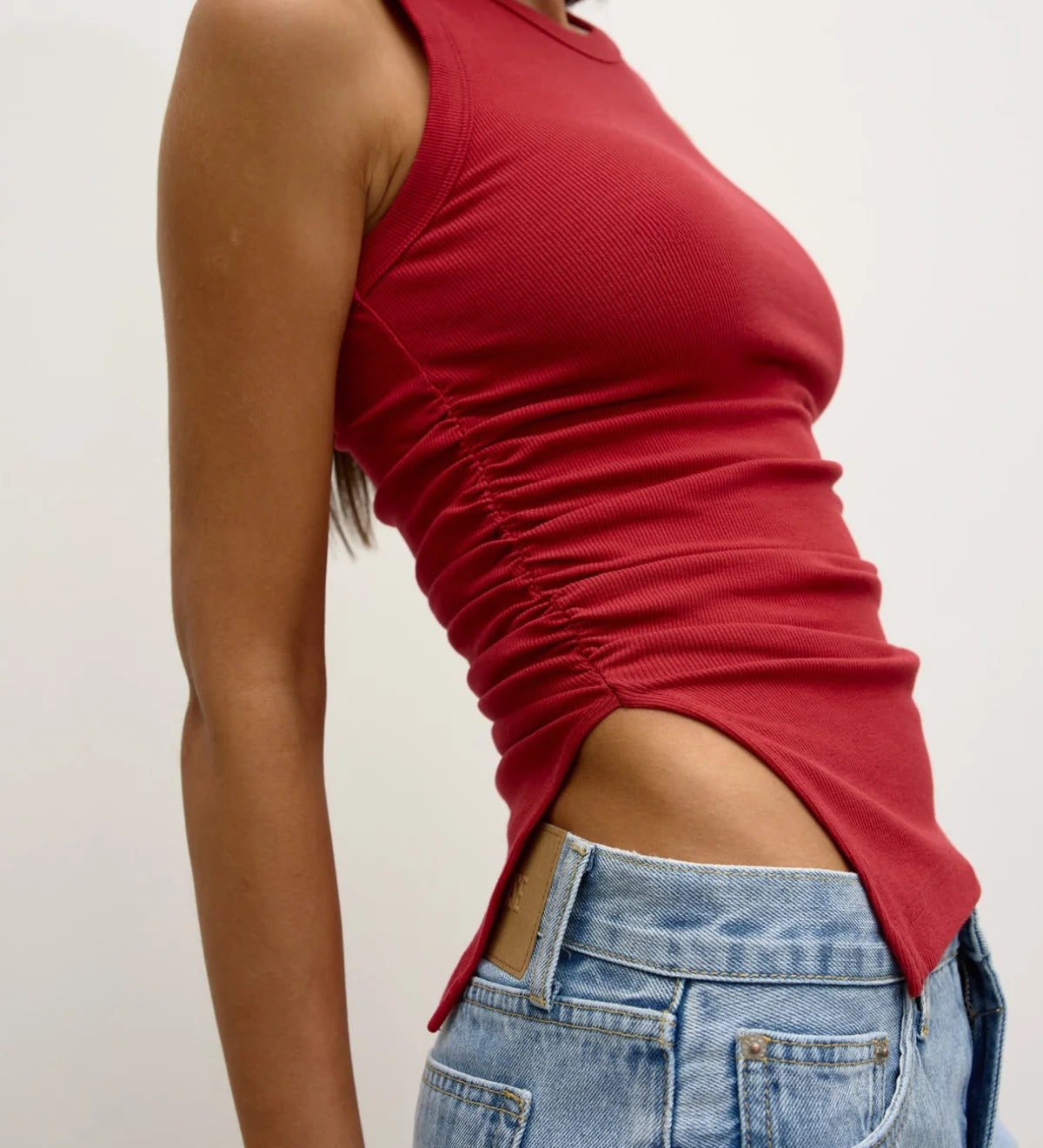 Person wearing a red sleeveless top and blue jeans against a plain background