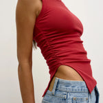 Person wearing a red sleeveless top and blue jeans against a plain background