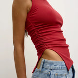 Person wearing a red sleeveless top and blue jeans against a plain background