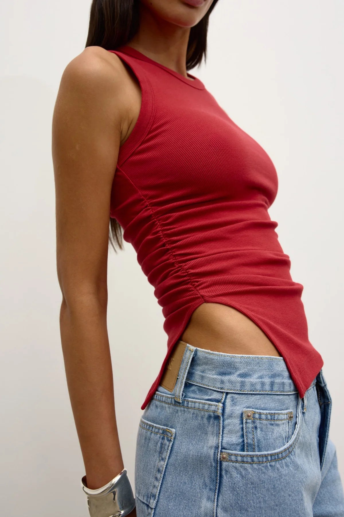 Person wearing a red sleeveless top and blue jeans against a plain background
