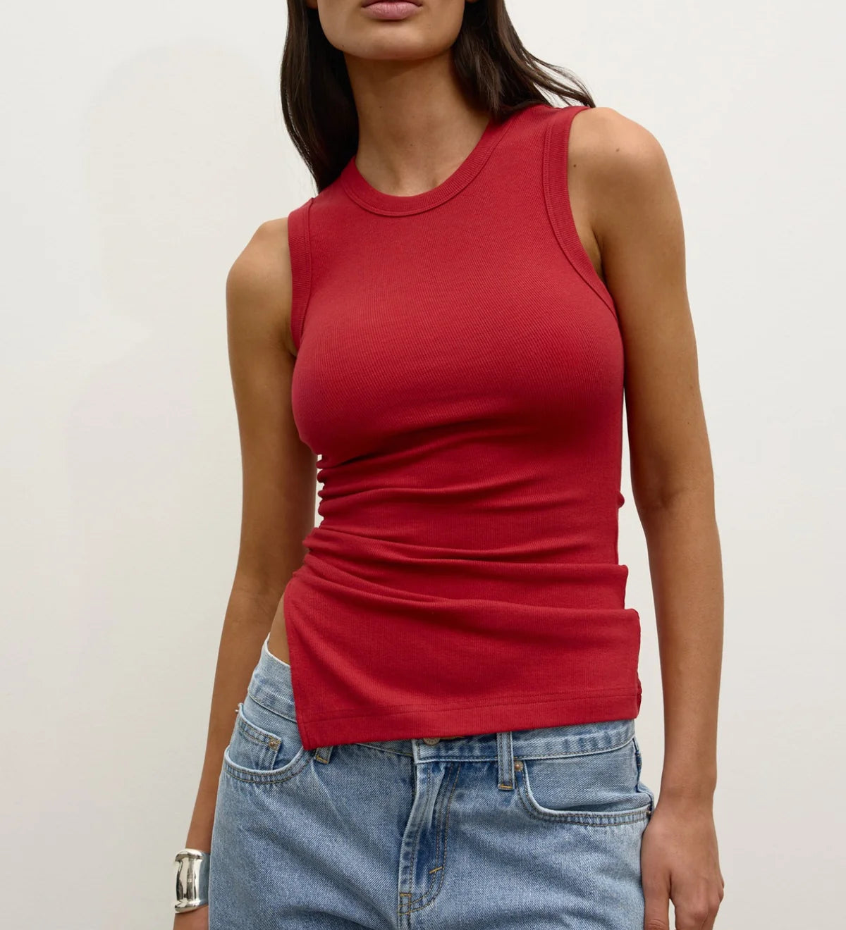 Woman wearing a red tank top and blue jeans against a plain background