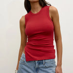 Woman wearing a red tank top and blue jeans against a plain background