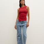 Woman wearing a red sleeveless top and light blue jeans against a white background