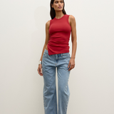 Woman wearing a red sleeveless top and light blue jeans against a white background