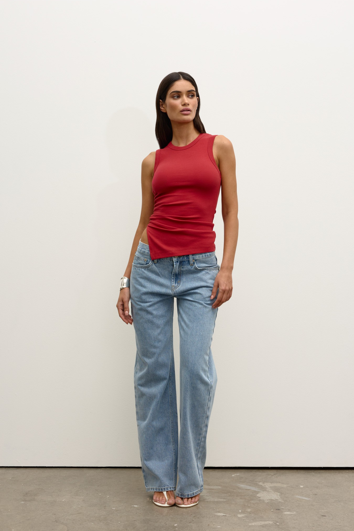 Woman wearing a red sleeveless top and light blue jeans against a white background