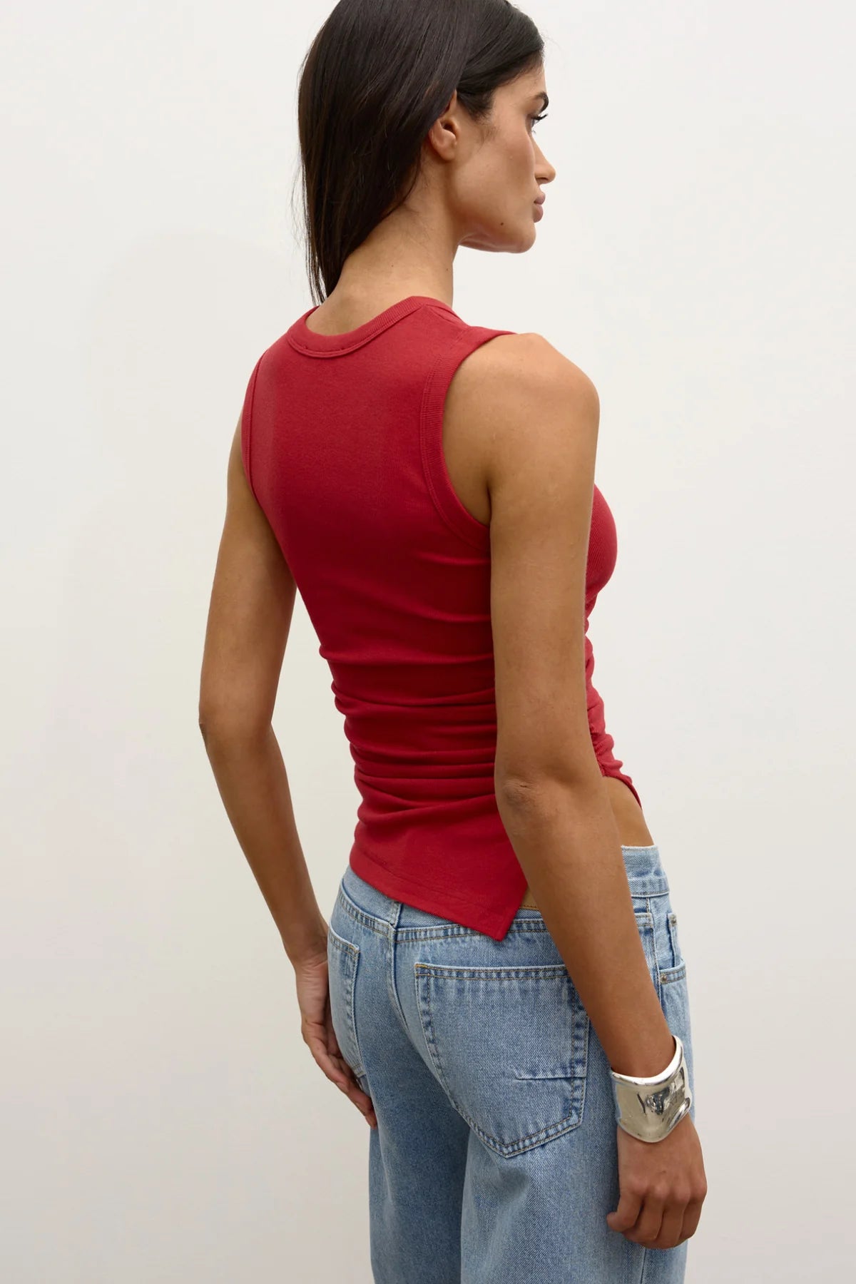 Woman wearing a red tank top and blue jeans against a white background