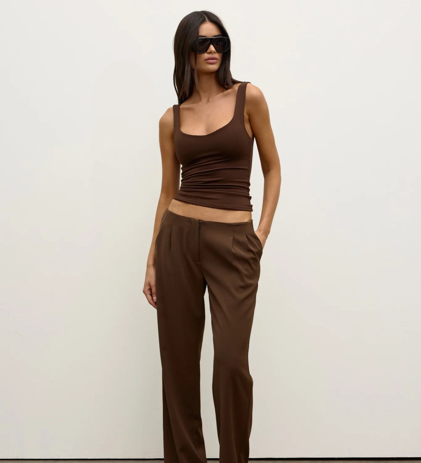 Woman wearing a brown tank top and high-waisted pants against a white background