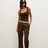 Woman wearing a brown tank top and high-waisted pants against a white background
