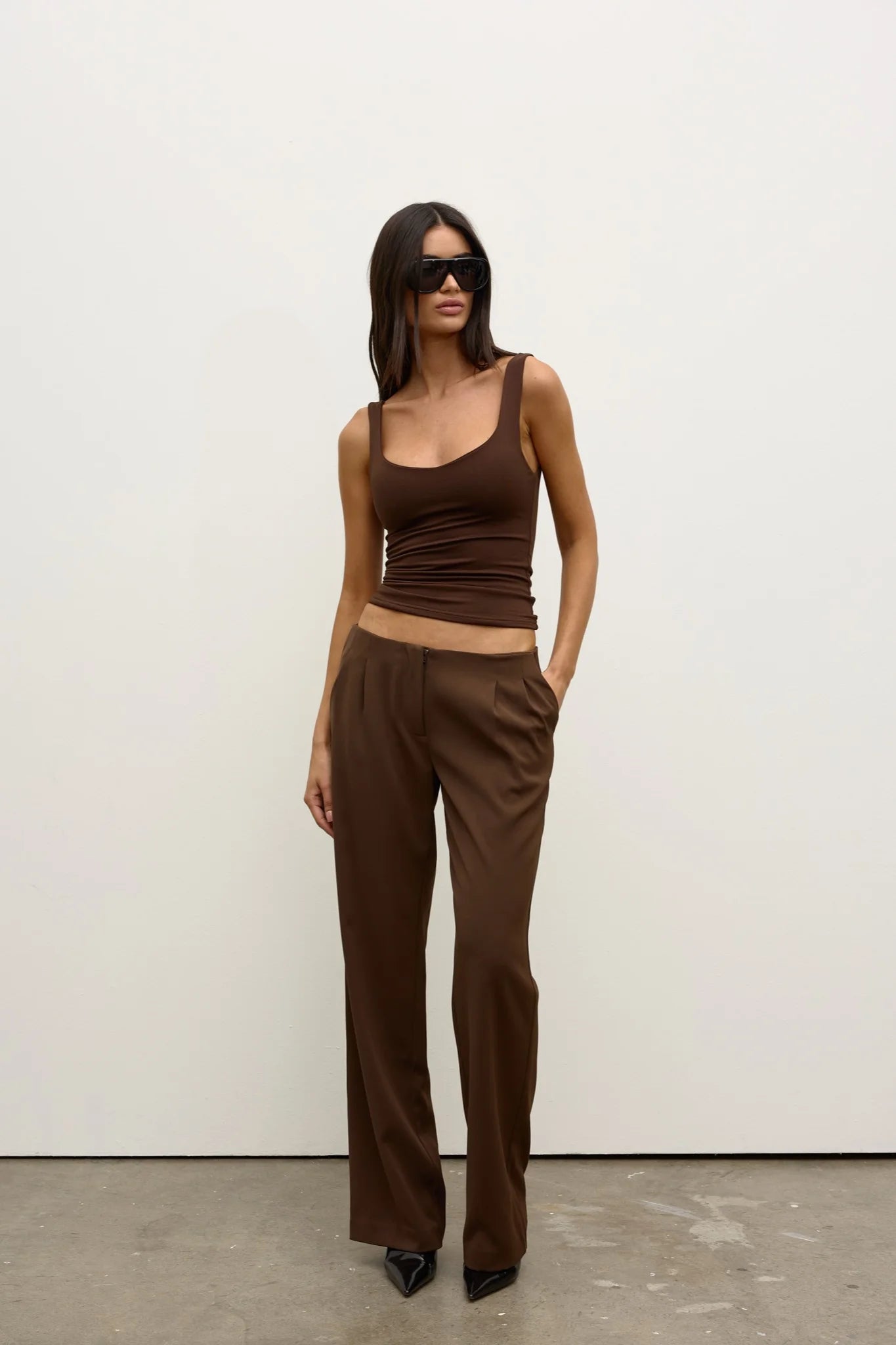 Woman wearing a brown tank top and high-waisted pants against a white background