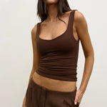 Woman wearing a brown tank top and pants with sunglasses on a plain background