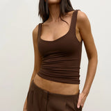 Woman wearing a brown tank top and pants with sunglasses on a plain background