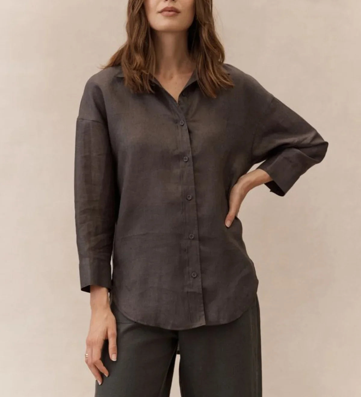 Woman wearing a dark brown shirt and pants against a beige background