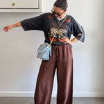 Person wearing a black sweater with a tiger design and brown pants, standing against a plain wall.