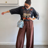 Person wearing a black sweater with a tiger design and brown pants, standing against a plain wall.