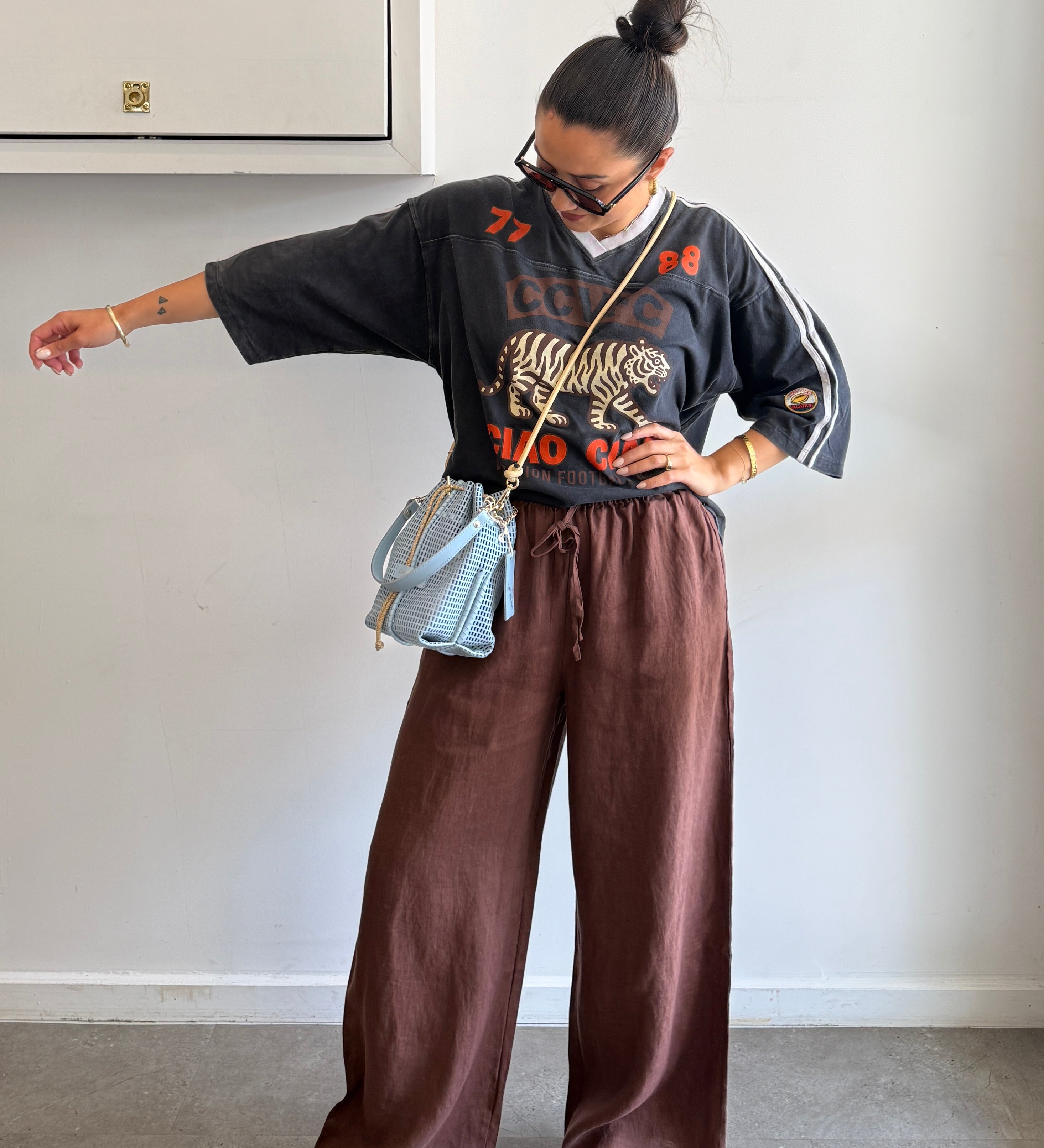 Person wearing a black sweater with a tiger design and brown pants, standing against a plain wall.