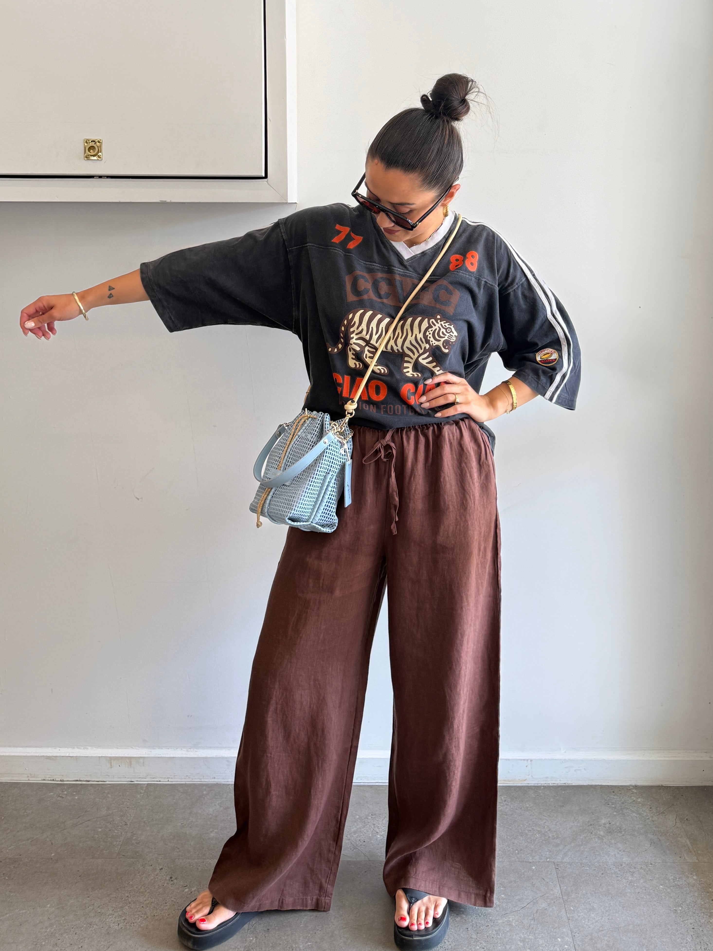 Person wearing a black sweater with a tiger design and brown pants, standing against a plain wall.