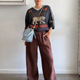 Person wearing a graphic t-shirt and brown pants indoors.