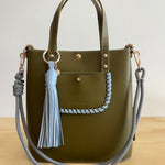 Green handbag with gray tassels and braided handle on a white background