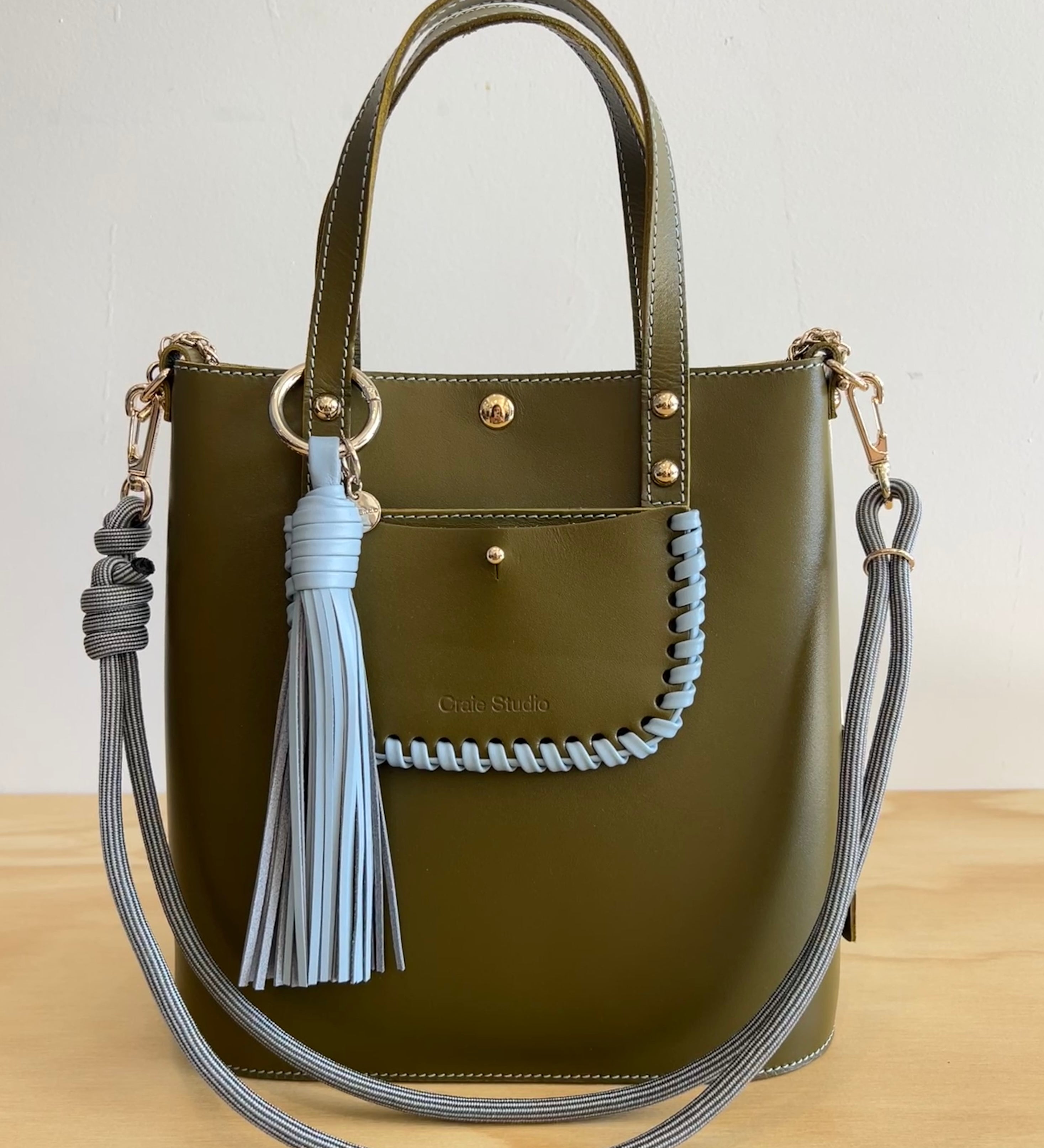 Green handbag with gray tassels and braided handle on a white background