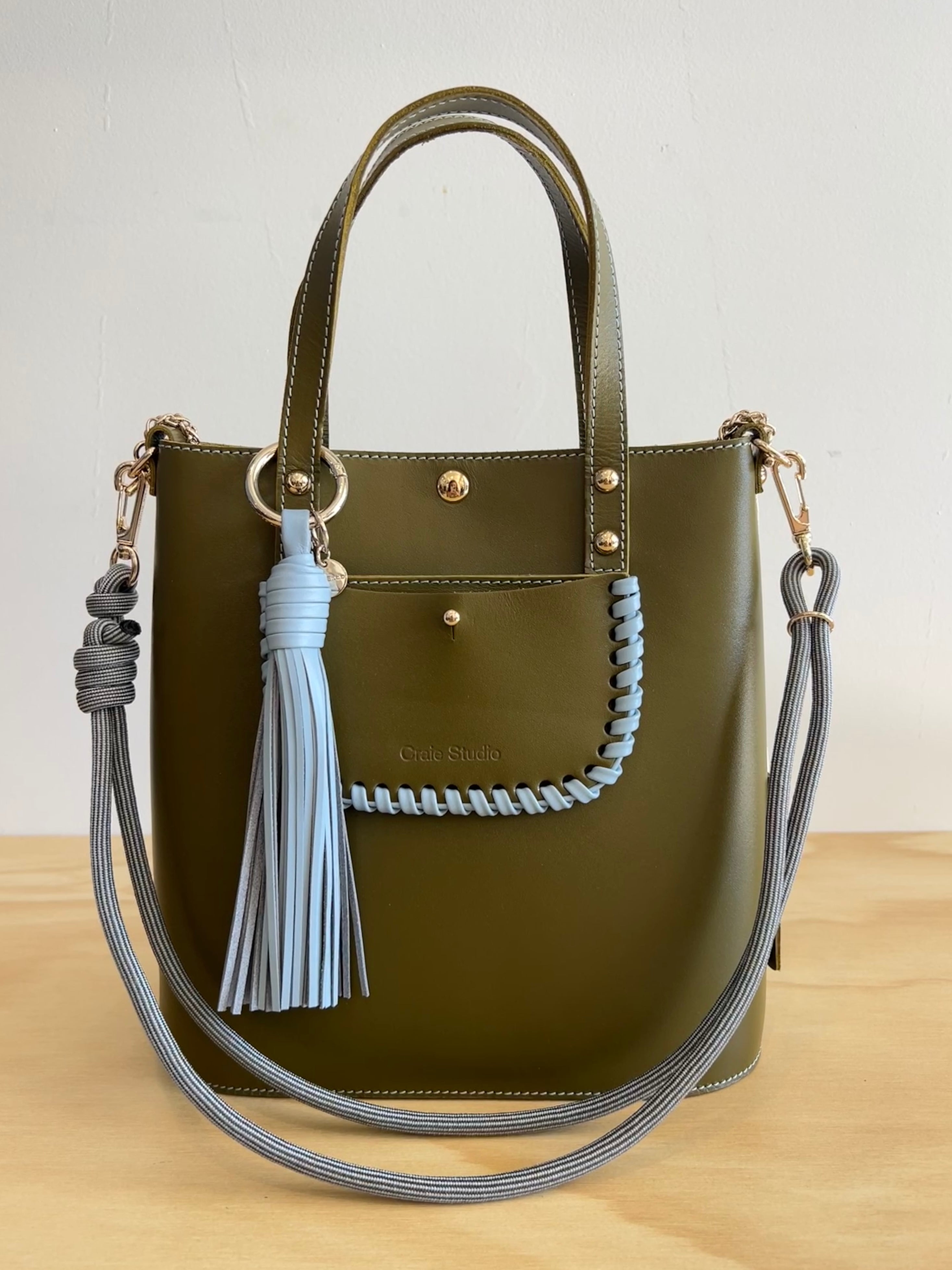 Green handbag with gray tassels and braided handle on a white background