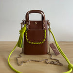Brown handbag with a green strap on a wooden surface