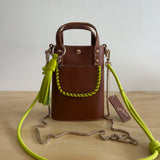 Brown handbag with a green strap on a wooden surface
