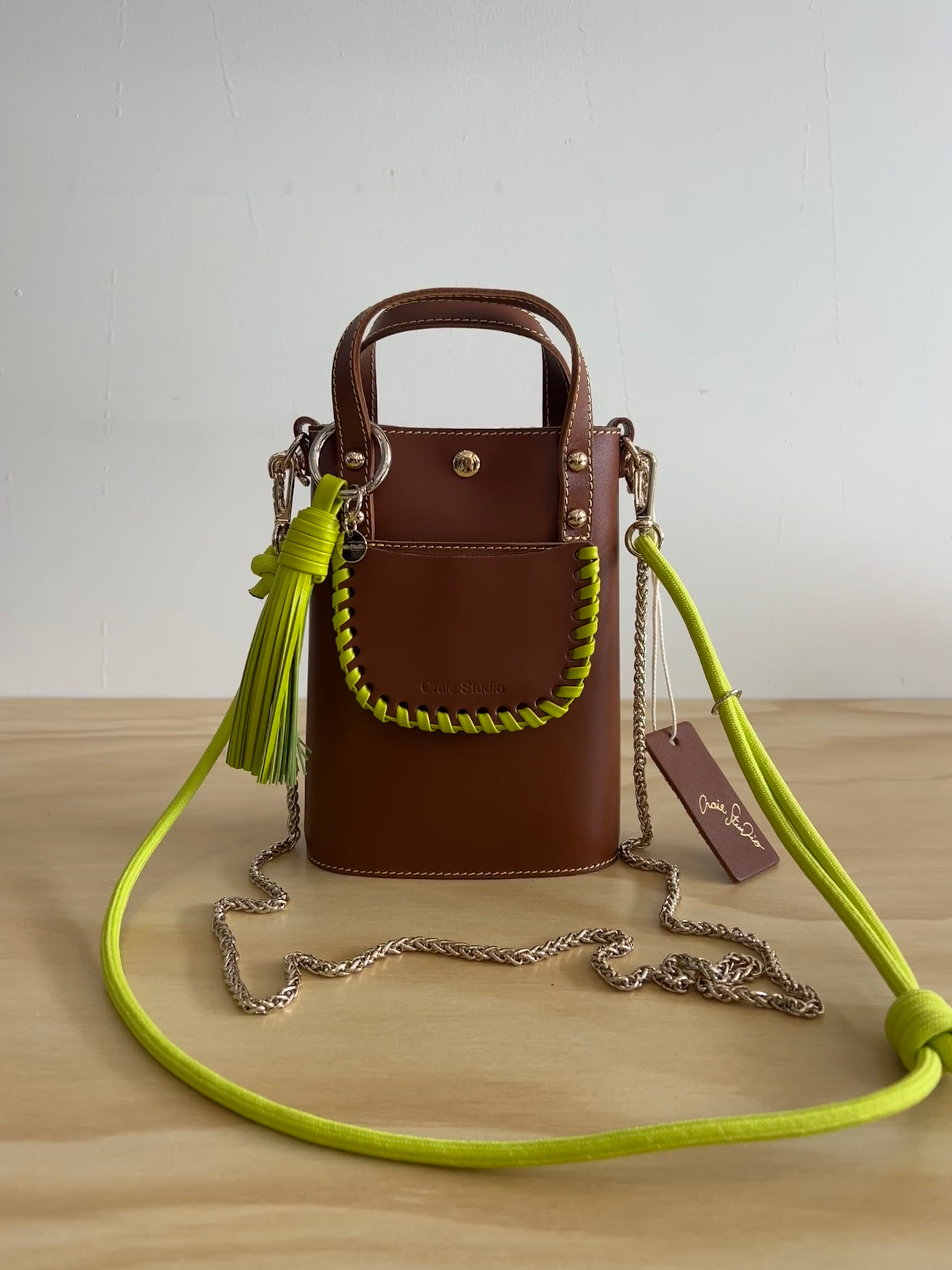 Brown handbag with a green strap on a wooden surface