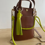 Brown handbag with green strap and tassel on a light background