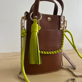 Brown handbag with green strap and tassel on a light background