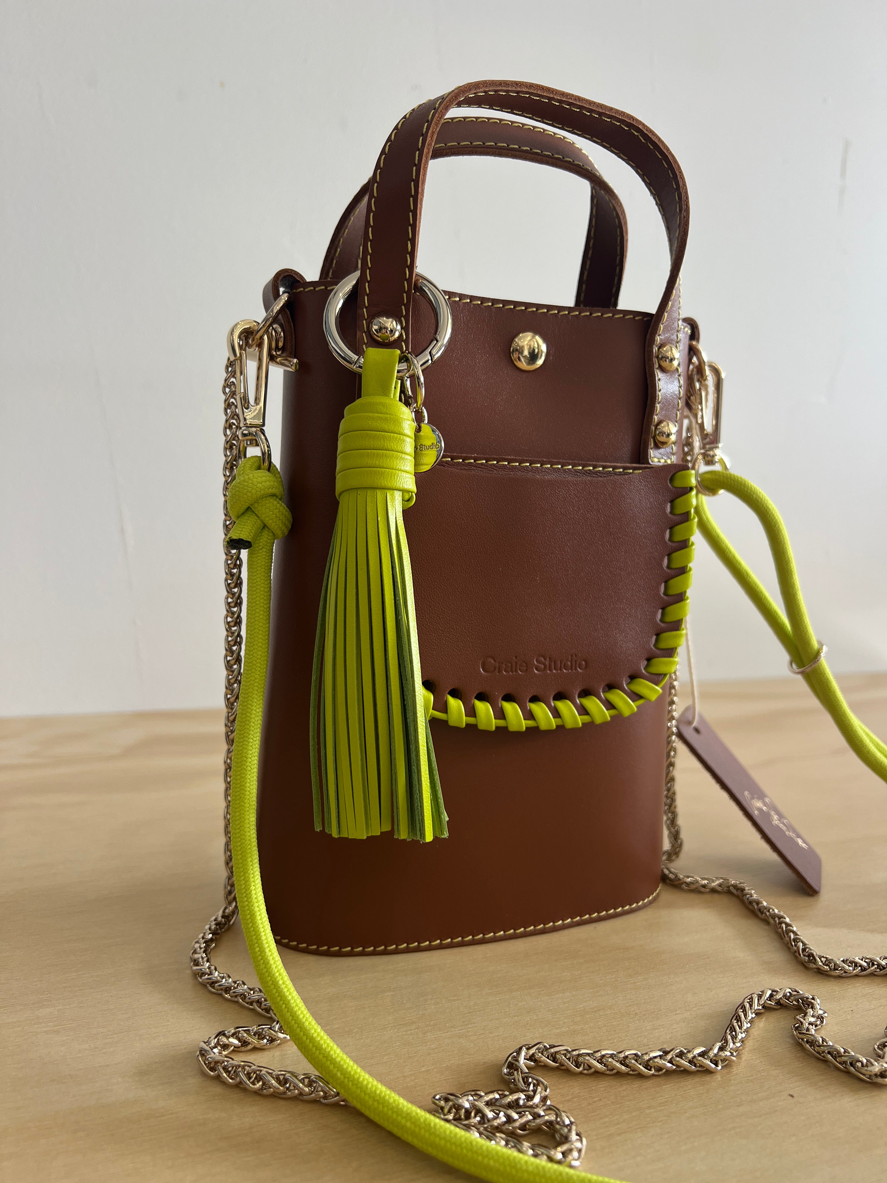 Brown handbag with green strap and tassel on a light background