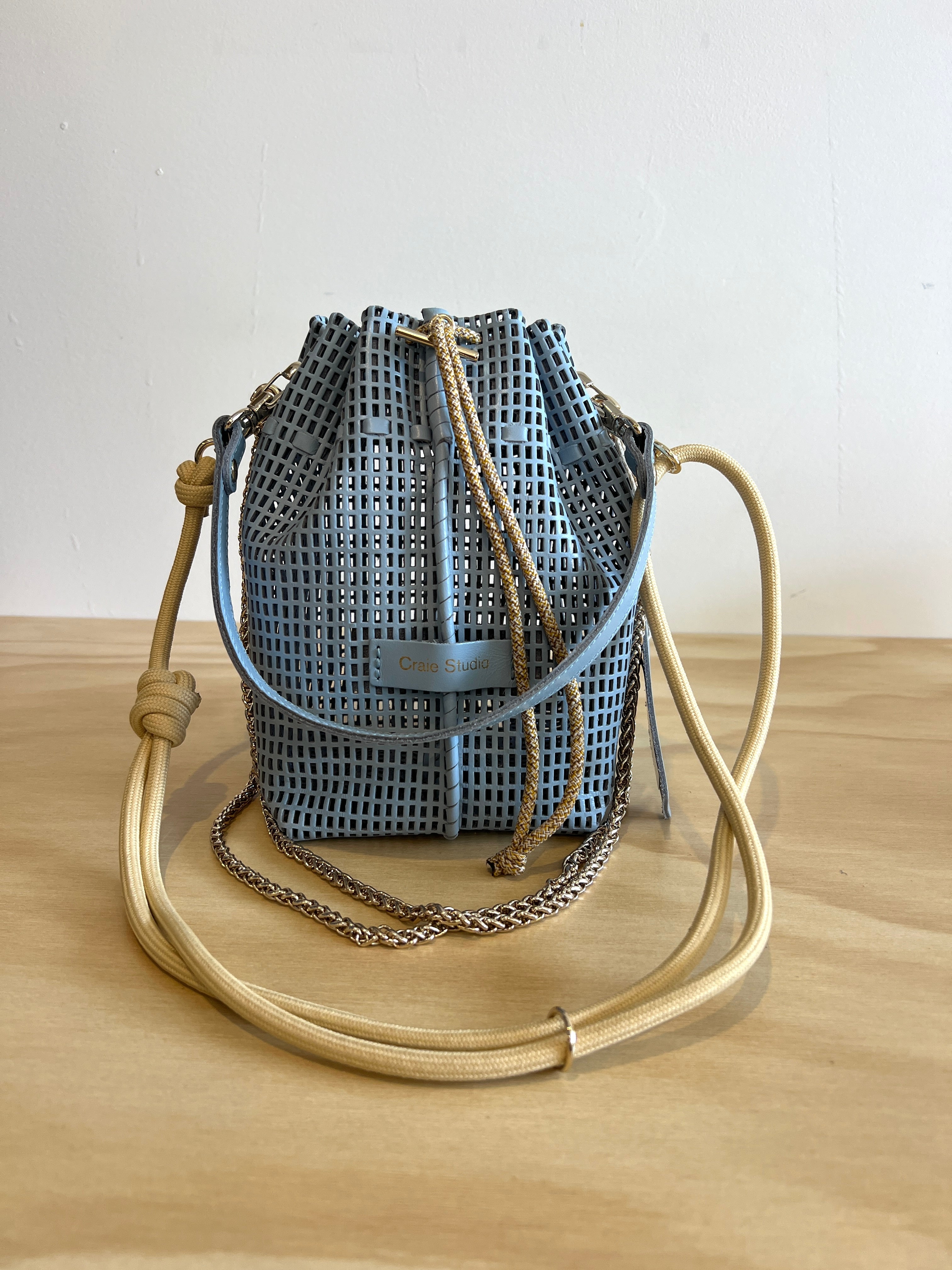 Woven bucket bag with beige handle on a wooden surface
