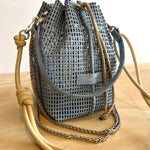Blue woven drawstring bag with beige shoulder strap on a wooden surface